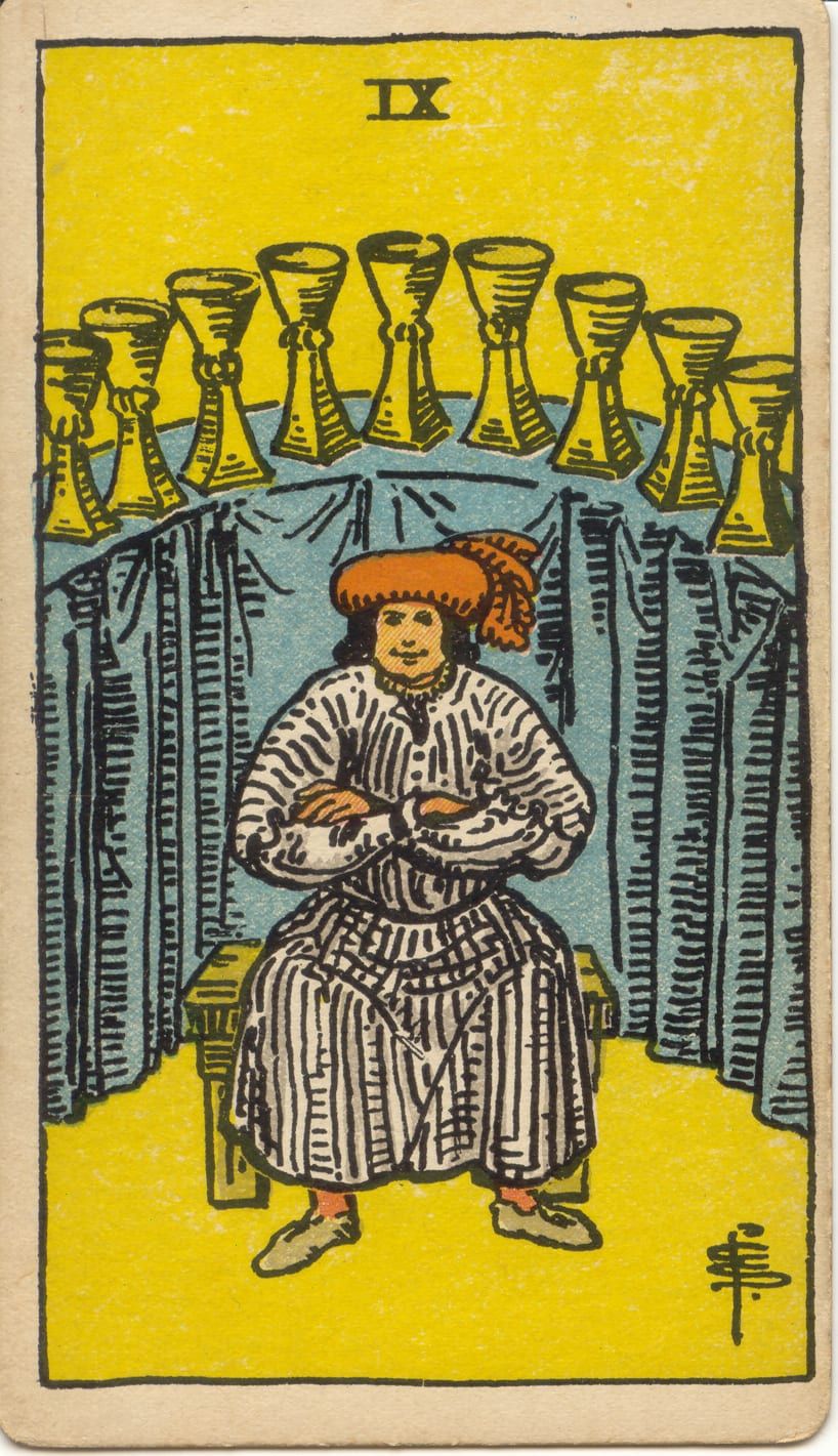 Карта Таро Девятка Кубков, 1909 год: довольный человек со скрещёнными руками сидит на скамье перед девятью кубками на голубом столе